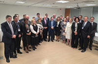 Foto mostra um grupo de pessoas, entre homens e mulheres. Todos estão em pé e posicionados em uma sala.