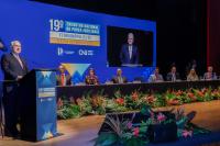 Foto mostra, um homem em pé, posicionado em um pulpito. Ao lado direito, pessoas sentadas em uma mesa de honra. Ao fundo, a informação: 19º Encontro Nacional do Poder Judiciário.
