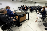 Foto mostra pessoas sentadas em um auditório em uma reunião.