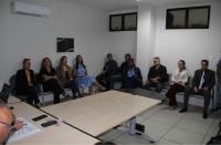 Foto mostra um grupo de pessoas, entre homens e mulheres sentados em uma sala de audiências