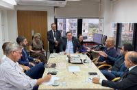 Foto mostra uma reunião de pessoas. Todos estão sentados em volta de uma mesa.