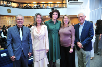 Foto mostra cinco pessoas em pé, uma ao lado do outra, dentro de um auditório. 