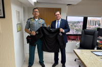 Foto mostra dois homens em pé, um ao lado do outro. Eles seguram uma camisa de combate. 