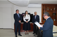 Foto mostra um homem no primeiro plano em pé lendo um documento. Ao fundo outros dois homens e uma mulher estão em pé.