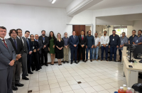 Foto mostra várias pessoas em pé, uma ao lado da outra. Todas estão na área interna de uma sala