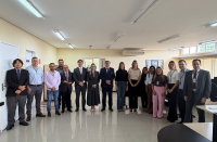 Foto mostra várias pessoas reunidas e uma sala. Todos estão em pé, um ao lado do outro.