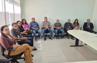Foto mostra homens e mulheres sentados. Todos estão em uma sala