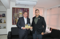Foto mostra dois homens em pé um ao lado do outro. Ambos seguram uma placa comemorativa