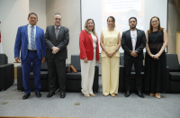 Foto mostra seis pessoas em pé, uma ao lado da outra dentro de um auditório