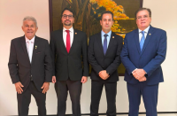 Foto mostra 4 homens usando terno escuro. Ambos estão em pé, um ao lado do outro