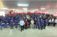 Foto mostra pessoas em pé dentro de um auditório.