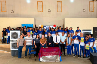 Foto mostra várias pessoas reunidas em um salão. Todos estão juntos em pé. São crianças, adolescentes e pessoas adultas reunidas.