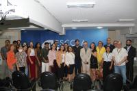 Foto mostra várias pessoas em pé uma ao lado da outra, dentro de um auditório. Ao fundo uma parede azul com no EJUD 16
