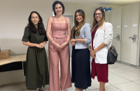 Foto mostra 4 mulheres uma ao lado da outra. Todas estão em pé e dentro de uma sala