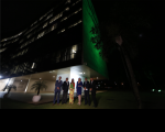 Foto de quatro homens e duas mulheres à frente da fachada do prédio do TST, iluminada de verde.