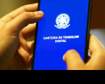 Foto de mãos segurando um celular. Na tela em fundo azul está escrito Carteira de Trabalho Digital em branco e o brasão da republica na mesma cor.