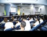 Imagem de um auditório com estudantes na plateia. Ao fundo, imagens do palestra Juiz Auxiliar da Corregedoria, Saulo Fontes.