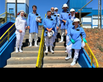 Foto de oito pessoas usando roupas de proteção e capacetes, posicionadas de pé numa escada de cimento com corrimãos amarelos. Todos posam para a câmera sorrindo.