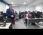 Imagens de pessoas sentadas em uma sala acompanhando uma palestra. Um homem usando um terno azul marinho e gravata vermelha está em pé.