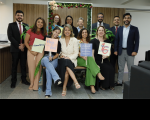 Foto de várias pessoas sorrindo e posando para a câmera, umas sentadas e outras em pé, num cenário decorado com flores.