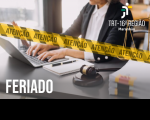 Recorte da foto de um homem, usando terno escuro e camisa social branca, digitando em um notebook que está sobre uma mesa. Em primeiro plano, faixa amarela na diagonal, onde se lê ATENÇÃO. No canto superior direito, logomarca do TRT-16 e no canto inferior esquerdo, texto escrito na cor branca FERIADO.