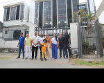 Foto de nove pessoas de pé e sorrindo para a câmera, e tendo ao fundo a fachada lateral do prédio-sede do TRT-16.