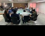Foto de mesa de reunião com várias pessoas em volta. 