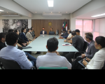 Foto mostra várias pessoas sentadas em volta de uma mesa de reuniões, durante audiência durante audiência de conciliação
