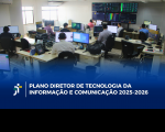 Foto mostra várias pessoas sentadas no ambiente de trabalho. Cada mesa, tem um computador sobre ela. Ao fundo, funciona uma painel com várias luzes coloridas. Na parte da baixo a informação: PLANO DIRETOR DE TECNOLOGIA DA INFORMAÇÃO E COMUNICAÇÃO 2025-2026
