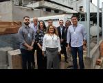 Foto mostra pessoas em pé, posicionadas em uma canteiro de obras. E ao fundo um gerador de energia. No centro da foto a Diretora-Geral Fernanda Muniz em sua volta servidores e servidoras. 
