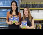 Foto mostra duas mulheres segurando cartilhas educativas do programa TRT na Escola
