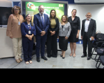 Foto mostra servidores e autoridades convidadas posicionadas de pé no auditório da Escola Judicial.