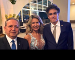 Foto mostra uma mulher posicionada ao lado de dois homens. Ambos estão com traje social.