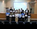 Foto mostra várias pessoas em pé, em um auditório. Todas seguram um certificado.