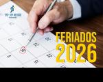 Arte feita com imagem de um calendário e uma mão de uma homem segura uma caneta marcando uma data. No canto inferior direito a informação: FERIADOS 2026