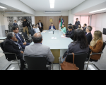 Foto mostra pessoas reunidades em volta de uma grande mesa de reunião.