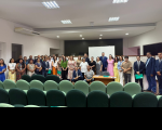 Foto mostra várias pessoas em pé, na parte de frente de um auditório.
