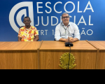 Foto mostra dois homens, sentados um ao lado do outro. Na parede do fundo, o nome Escola Judicial TRT16