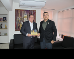 Foto mostra dois homens em pé um ao lado do outro. Ambos seguram uma placa comemorativa