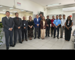 Foto mostra um grupo formado por homens e mulheres em pé. Um ao lado do outro. Ambos estão em uma sala.