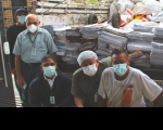 Foto mostra homens usando máscaras posicionados na frente de um caminha com material reciclável