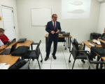 Foto mostra um homem usando um terno escuro, posicionado em pé no meio de uma sala de treinamento
