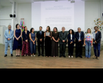Foto mostra um grupo de pessoas em pé no centro de um auditório.