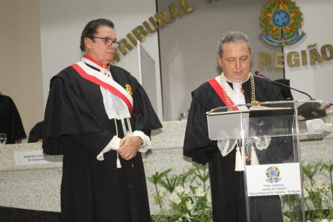 dois homens de toga em pé, estando um na tribuna lendo e o outro ao lado