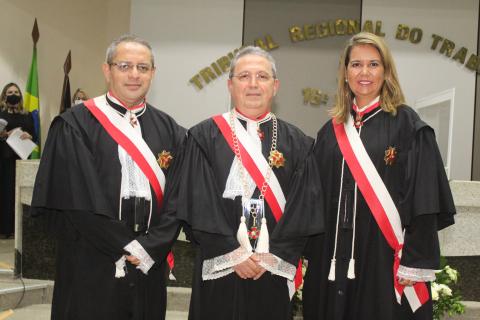 um homem de toga, no meio, entre um homem também de toga a direita e uma mulher de toga  a esquerda, pousando para foto