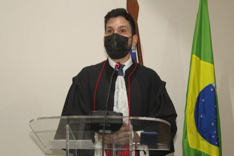homem de toga discursando em pé em frente a uma tribuna