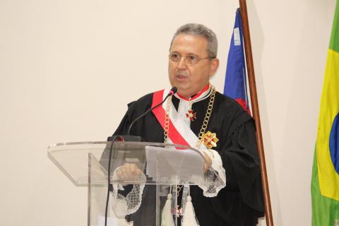 homem de toga discursando em pé em frente a uma tribuna