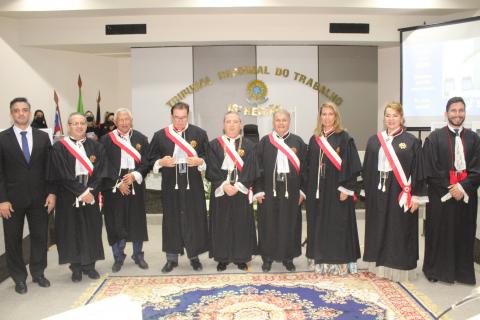 Nove pessoas em pé pousando para foto, sendo oito de toga e um de terno
