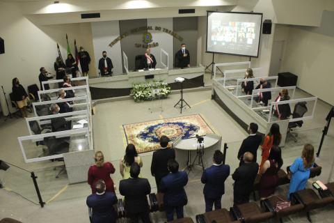 Espaço com pessoas em posição de respeito em volta a uma mesa com autoridades