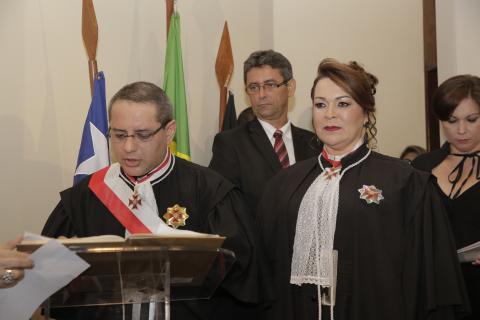 mulher de toga ao lado de homem de toga apoiado em uma tribuna assinando o ato de  posse